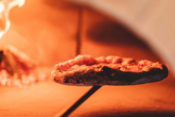 Pizza on long wooden peel in warm wood fired oven.