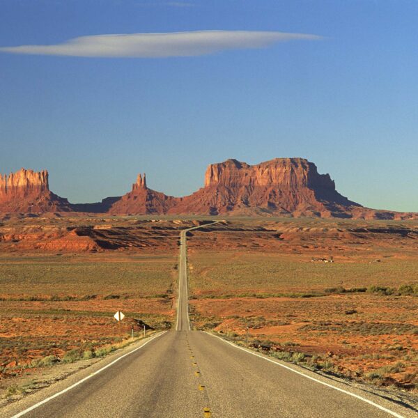 Red stone towers in desert setting with long straight highway.