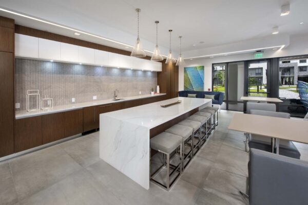 Community kitchen with large stone bar, plush stools, and wood style cabinets.