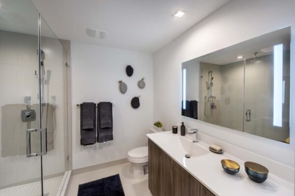 Bathroom with stone style counter, large mirror, and tiled shower.