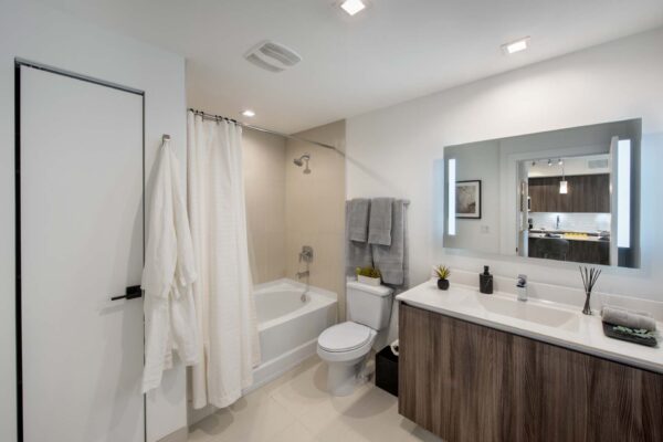Bathroom with wood style cabinet, stone counter, large mirror, and tiled shower tub.
