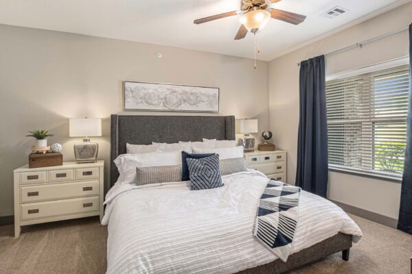 Bedroom with carpet, plush bed with headboard, bedside chests with lamps, and ceiling fan.