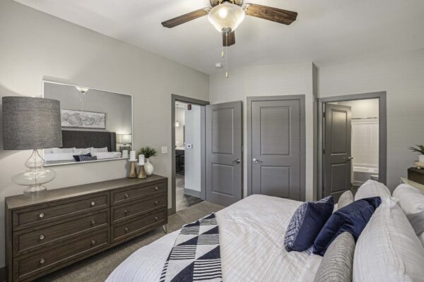 Bedroom with carpet, plush bed with pillows, dresser with lamp and decor, and large mirror.