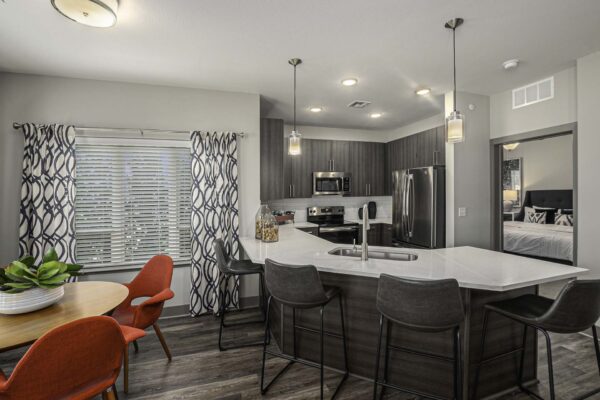 Apartment kitchen with wood style floor and cabinets, dining table, and stainless steel appliances.