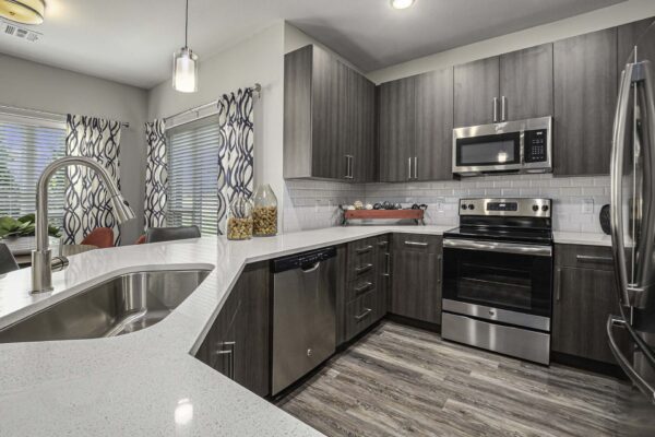 Apartment kitchen with wood style floor and cabinets, light counters, and stainless steel appliances.