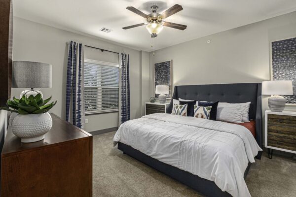 Bedroom with carpet, plush bed with headboard, bedside drawers with lamps, and large window.