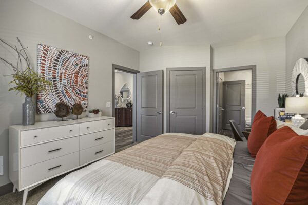 Bedroom with plush bed, dresser with decor, large artwork, and door to bathroom.