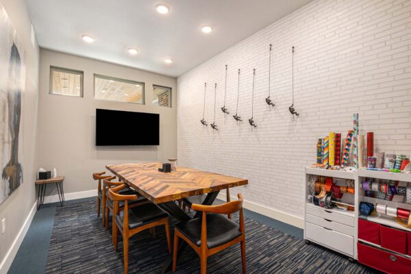 Craft room with pattern rug, wood table and chairs, wall mounted TV, and craft supplies.
