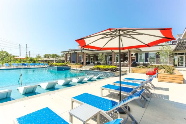 Pool area with lounge chairs, umbrellas, and lush planters.