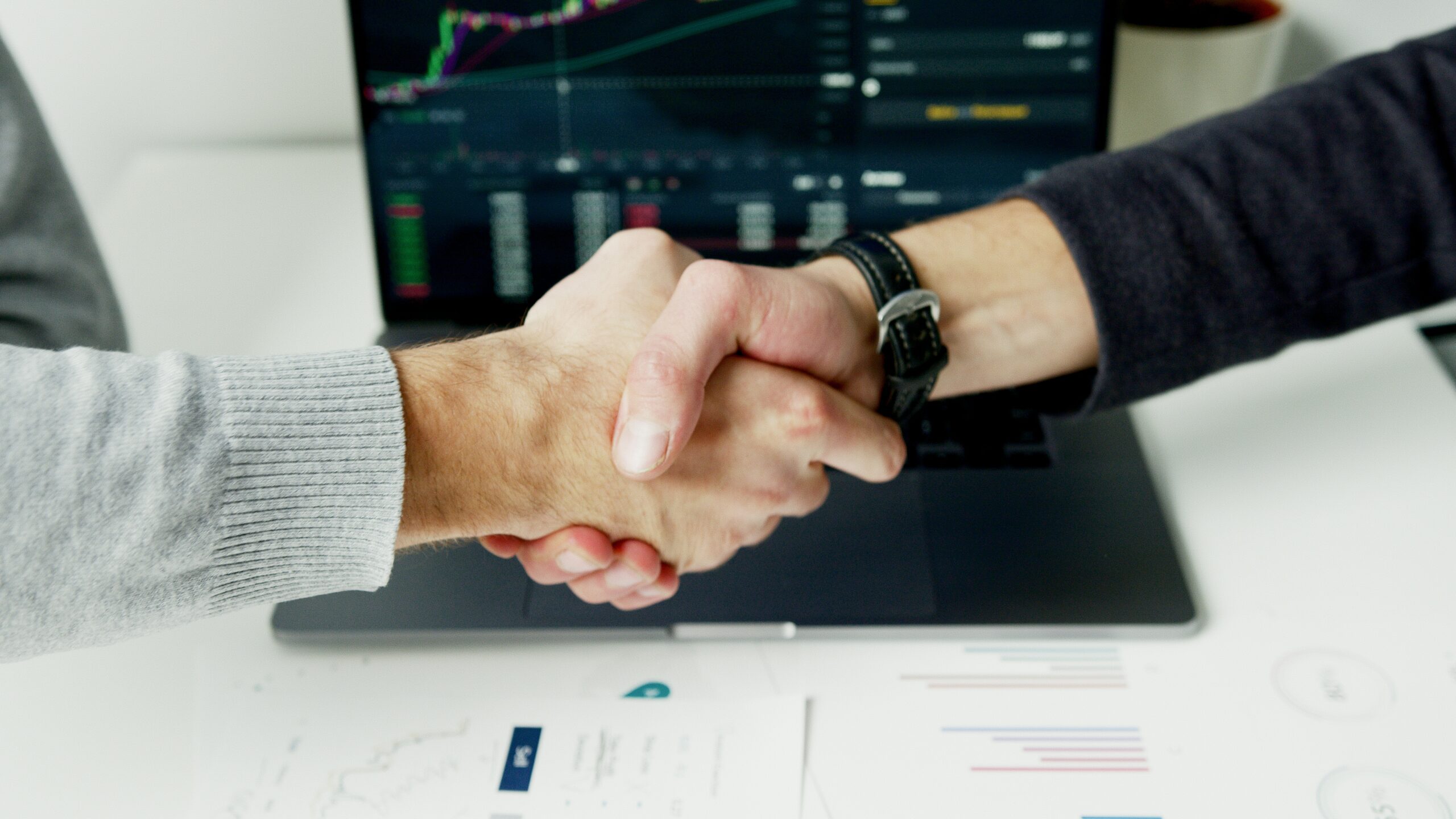 Coworkers shaking hands in front of computer screen.