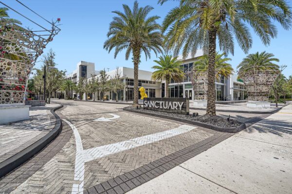 Sanctuary Doral apartments drive way with large monument sign and tall palm trees.