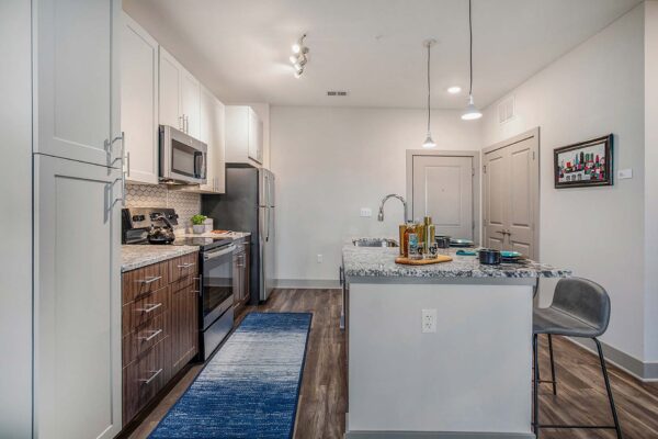 Arte KC apartment kitchen with wood style floor and cabinets, stone counters, and stainless steel appliances.