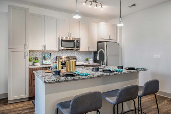 Arte KC apartment kitchen with wood style floor and cabinets, stone counters, and stainless steel appliances.