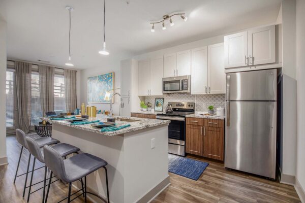 Arte KC apartment kitchen with wood style floor and cabinets, stone counters, and stainless steel appliances.