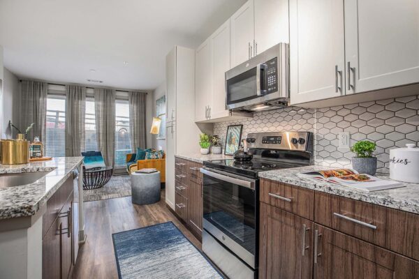 Arte KC apartment kitchen with wood style floor and cabinets, stone counters, and stainless steel appliances.