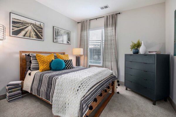 Arte KC apartment bedroom with plush carpet, wood bed with headboard, and large windows.