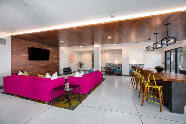 Arte KC apartments clubroom with stone floors, plush pink couches, dining bar with stools, and TV.