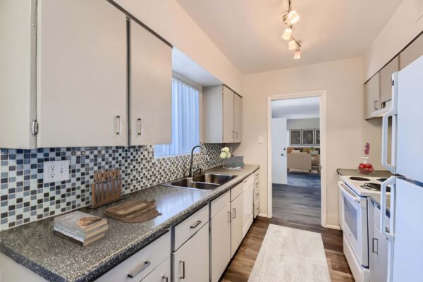 Aura at Midtown apartment kitchen with wood style floor, white cabinets, tiled backsplash, and white appliances.