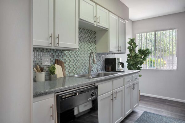 Aura at Midtown apartment kitchen with white cabinets, tiled backsplash, and stainless steel sink.
