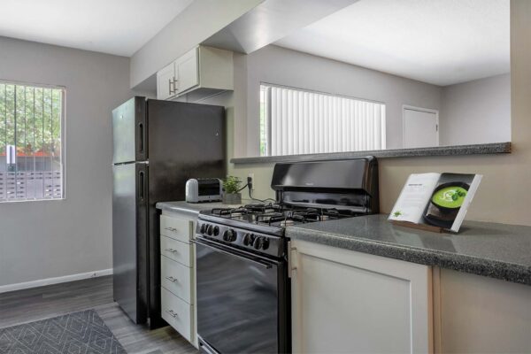 Aura at Midtown apartment kitchen with white cabinets, black appliances, and opening to living room.