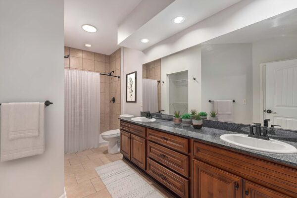 Highlands Lodge apartment bathroom with tile floor, wood cabinets, stone counters, and tiled shower.