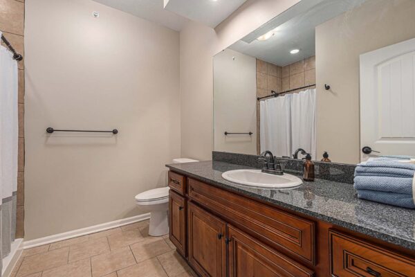 Highlands Lodge apartment bathroom with tile floor, wood cabinets, stone counters, and large mirror.