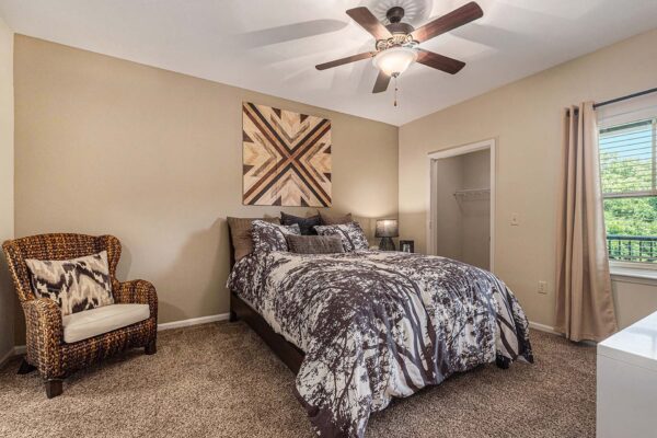 Highlands Lodge apartment bedroom with plush carpet, large bed with pillows, armchair, and ceiling fan.