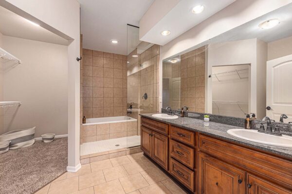 Highlands Lodge apartment bathroom with tile floor, wood cabinets, stone counters, and tiled shower and tub.