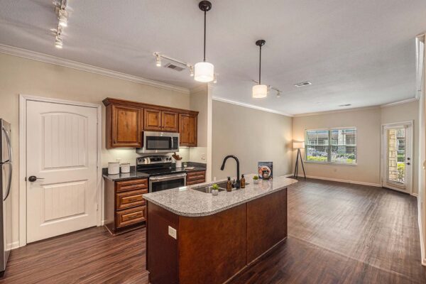 Highlands Lodge apartment kitchen with wood style floor and cabinets, dark stone counters, and stainless steel appliances.