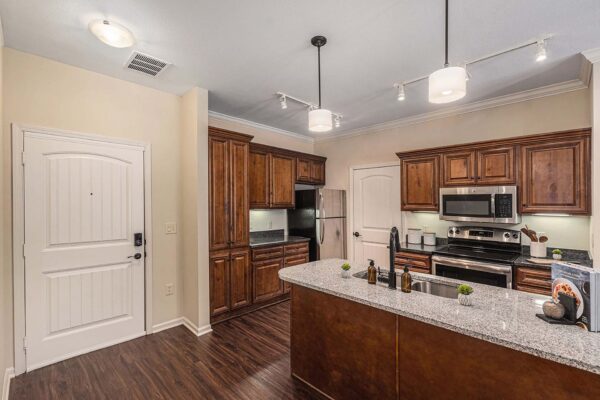 Highlands Lodge apartment kitchen with wood style floor and cabinets, dark stone counters, and stainless steel appliances.