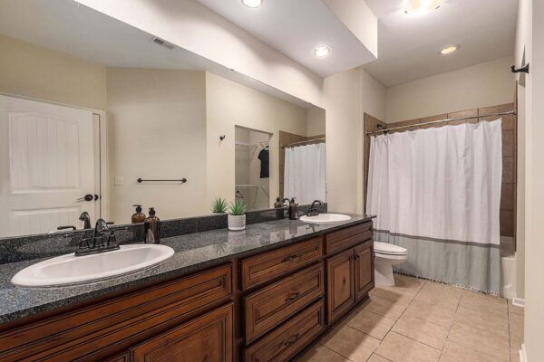 Highlands Lodge apartment bathroom with tile floor, wood cabinets, dark stone counters, and tiled shower tub.