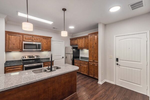 Highlands Lodge apartment kitchen with wood style floor and cabinets, stone counters, and stainless steel appliances.