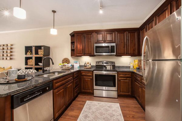 Highlands Lodge apartment kitchen with wood style floor and cabinets, stone counters, and stainless steel appliances.