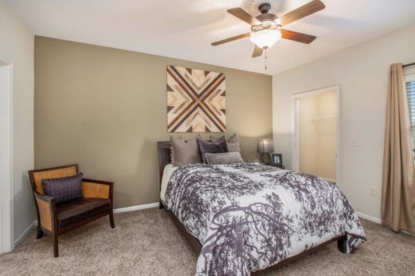 Highlands Lodge apartment bedroom with carpet, plush bed with headboard, large artwork, and ceiling fan.