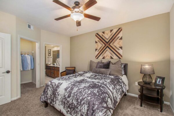 Highlands Lodge apartment bedroom with carpet, plush bed with headboard, large artwork, and ceiling fan.