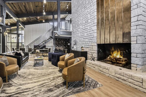 Kenilworth apartments clubhouse with plush seating, metal and stone fireplace, and stairs to mezzanine.