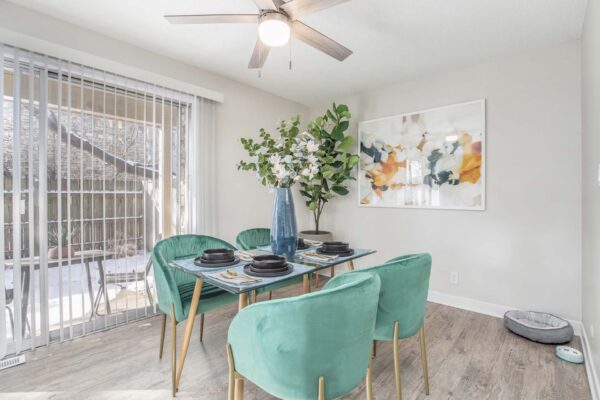 Kenilworth apartment dining room with wood style floor, dining table with green velvet chairs, and balcony door.
