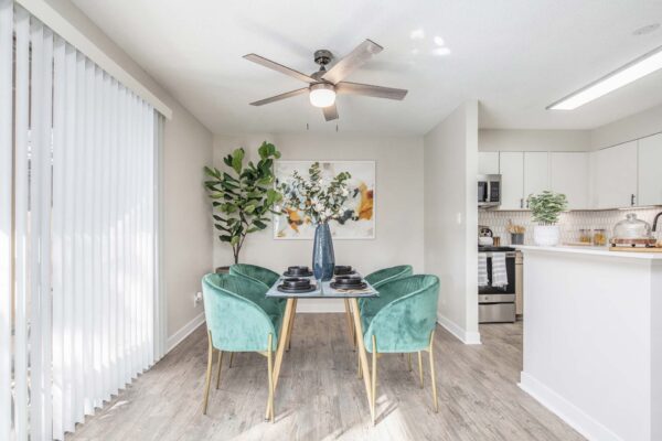 Kenilworth apartment dining room with wood style floor, dining table with green velvet chairs, and balcony door.