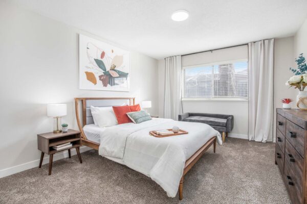 Kenilworth apartment bedroom with plush carpet, wood bed with headboard, bedside tables with lamps, and large window.