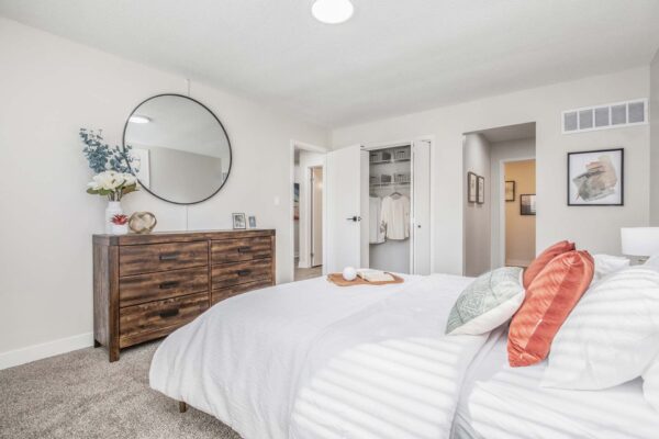 Kenilworth apartment bedroom with plush carpet, wood bed with headboard, dresser with flowers, and round mirror.