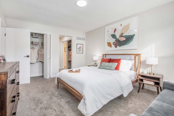 Kenilworth apartment bedroom with plush carpet, wood bed with headboard, bedside tables with lamps, and closet.