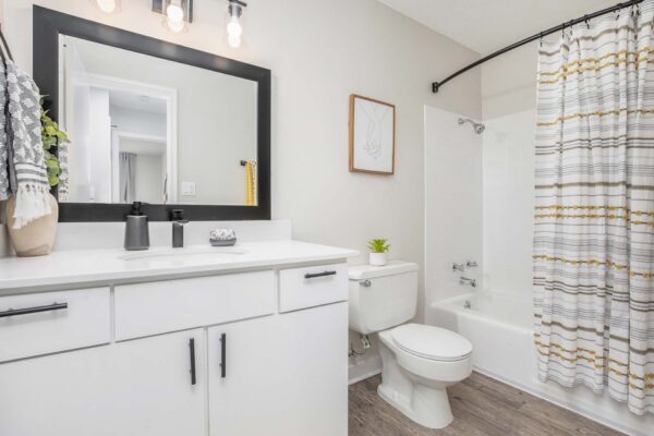 Kenilworth apartment bathroom with wood style floor, white cabinets and counters, and tiled shower tub.