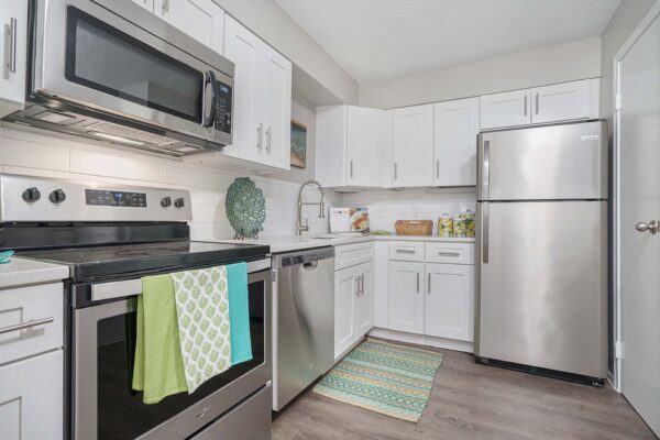 Kenilworth apartment kitchen with wood style floor, white cabinets and counters, and stainless steel appliances.