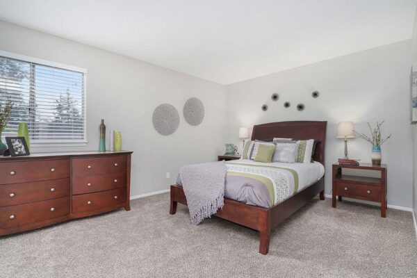 Kenilworth apartment bedroom with plush carpet, wood bed with headboard, dresser with decor and photos.