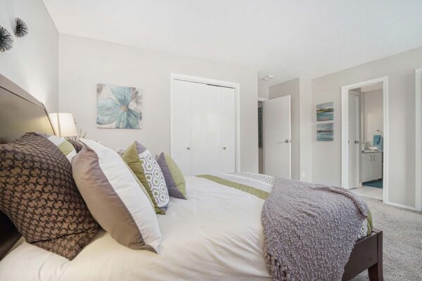 Kenilworth apartment bedroom with plush carpet, wood bed with headboard, and closet door.