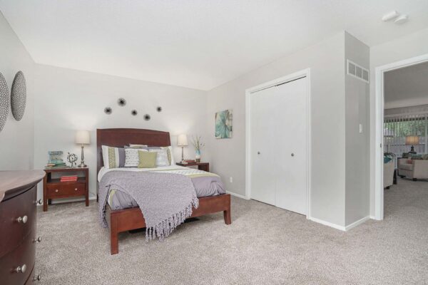Kenilworth apartment bedroom with plush carpet, wood bed with headboard, and bedside tables with lamps.