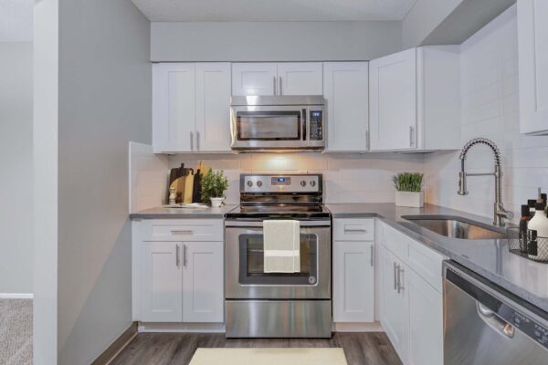 Kenilworth apartment kitchen with wood style floor, white cabinets, tiled backsplash, and stainless steel appliances.