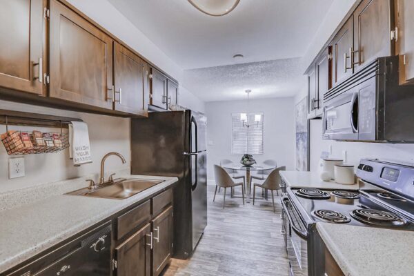 Latitude apartment kitchen with wood style floor and cabinets, light counters, and black appliances.