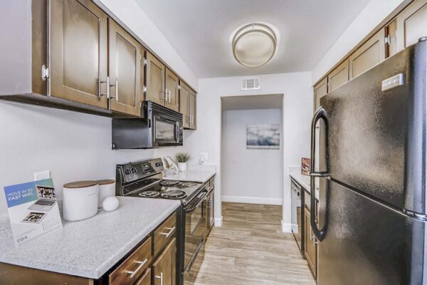 Latitude apartment kitchen with wood style floor and cabinets, light counters, and black appliances.