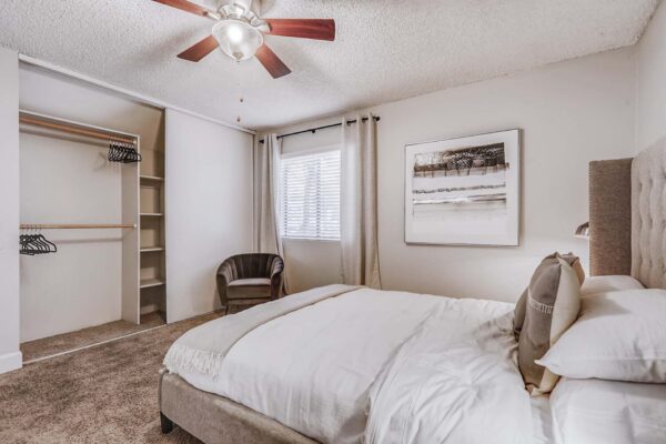 Latitude apartment bedroom with carpet, plush bed with headboard, bedside tables with lamps, and large window.